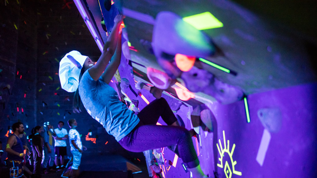 UAF student concentrates on the glowing flourecent rocks as she climbs the rocking climbing wall under UV light